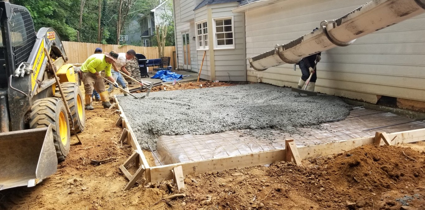 Concrete crew preparing gravel base for residential patio installation